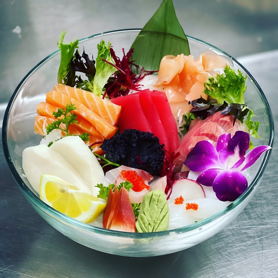 A colorful Saisaki sushi and sashimi platter in a glass bowl with a purple orchid garnish.