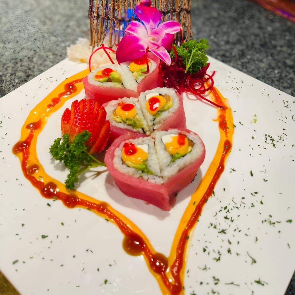 Heart-shaped Saisaki sushi rolls with mango, avocado, and red sauce, garnished with a pink orchid.