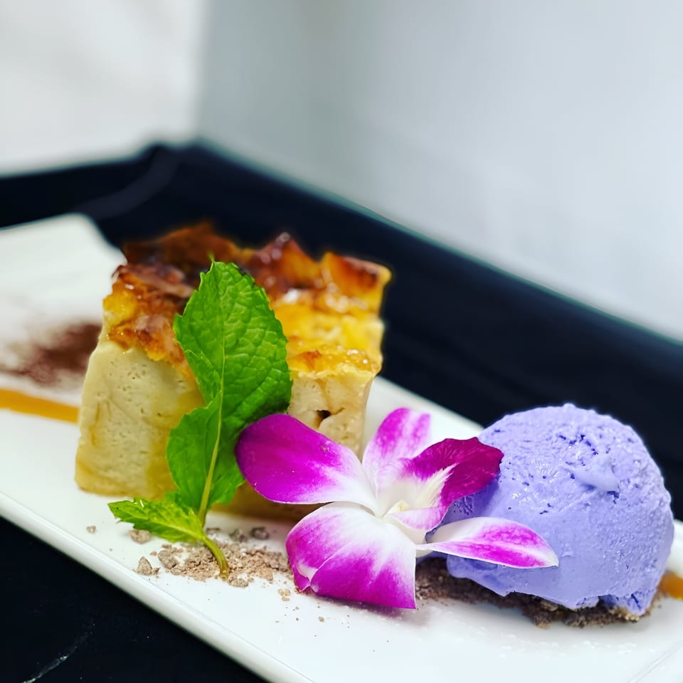 Saisaki dessert with a slice of cake, purple ice cream, mint, and an orchid on a white plate.