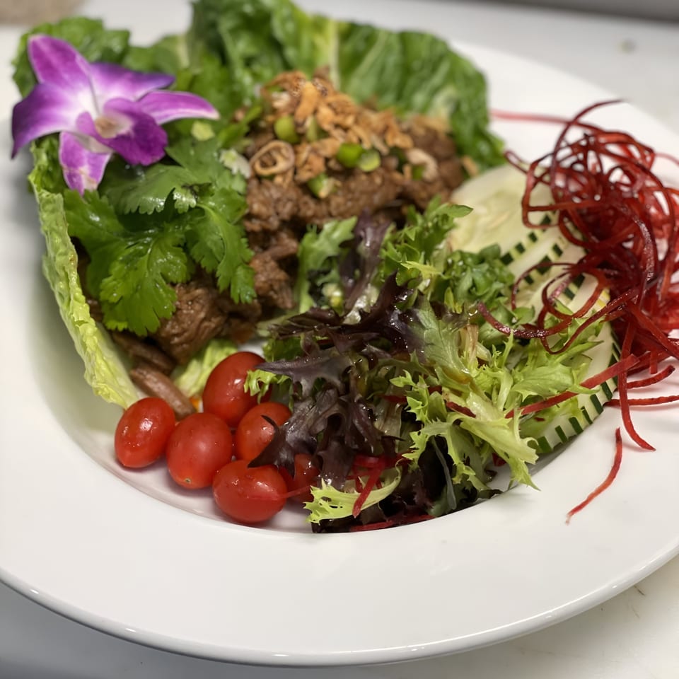 A vibrant Saisaki salad with beef, mixed greens, cherry tomatoes, cucumbers, and a purple orchid garnish.