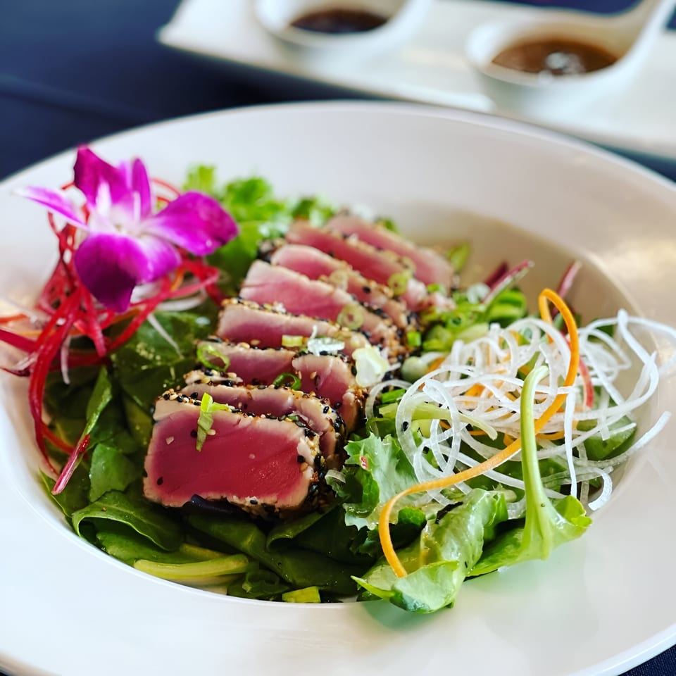 Seared tuna sashimi salad with mixed greens, shredded vegetables, and a purple orchid garnish.