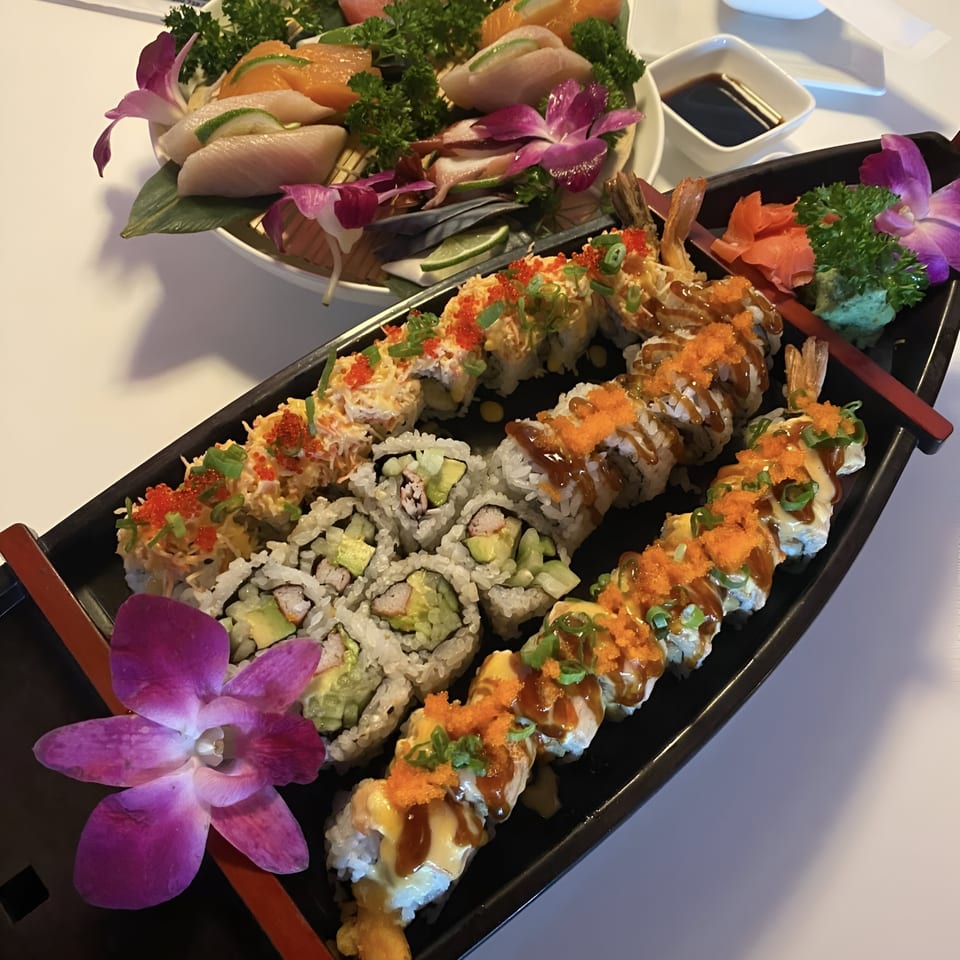 A sushi boat with various rolls, sashimi, and purple orchids on a white table.