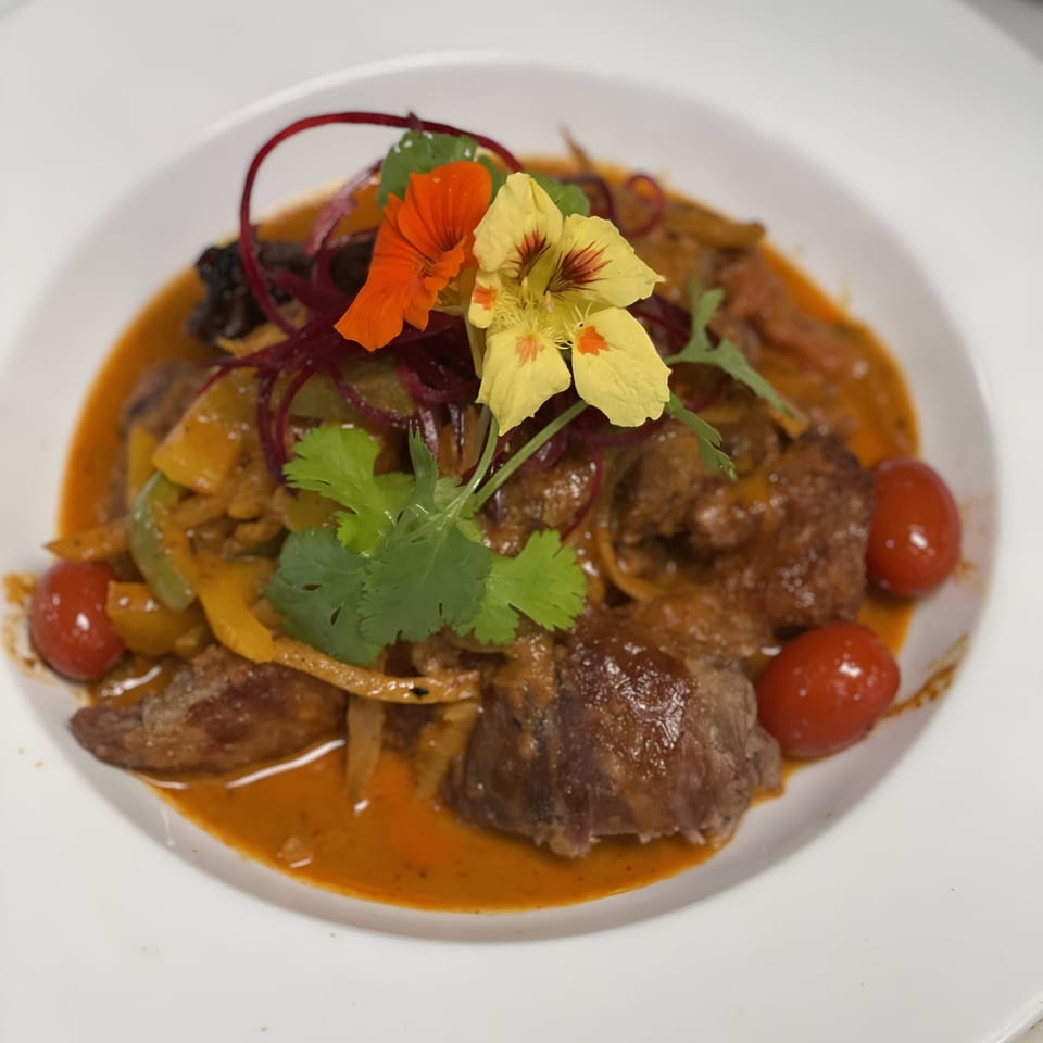 A dish with meat, vegetables, cherry tomatoes, and edible flowers in a rich orange sauce.