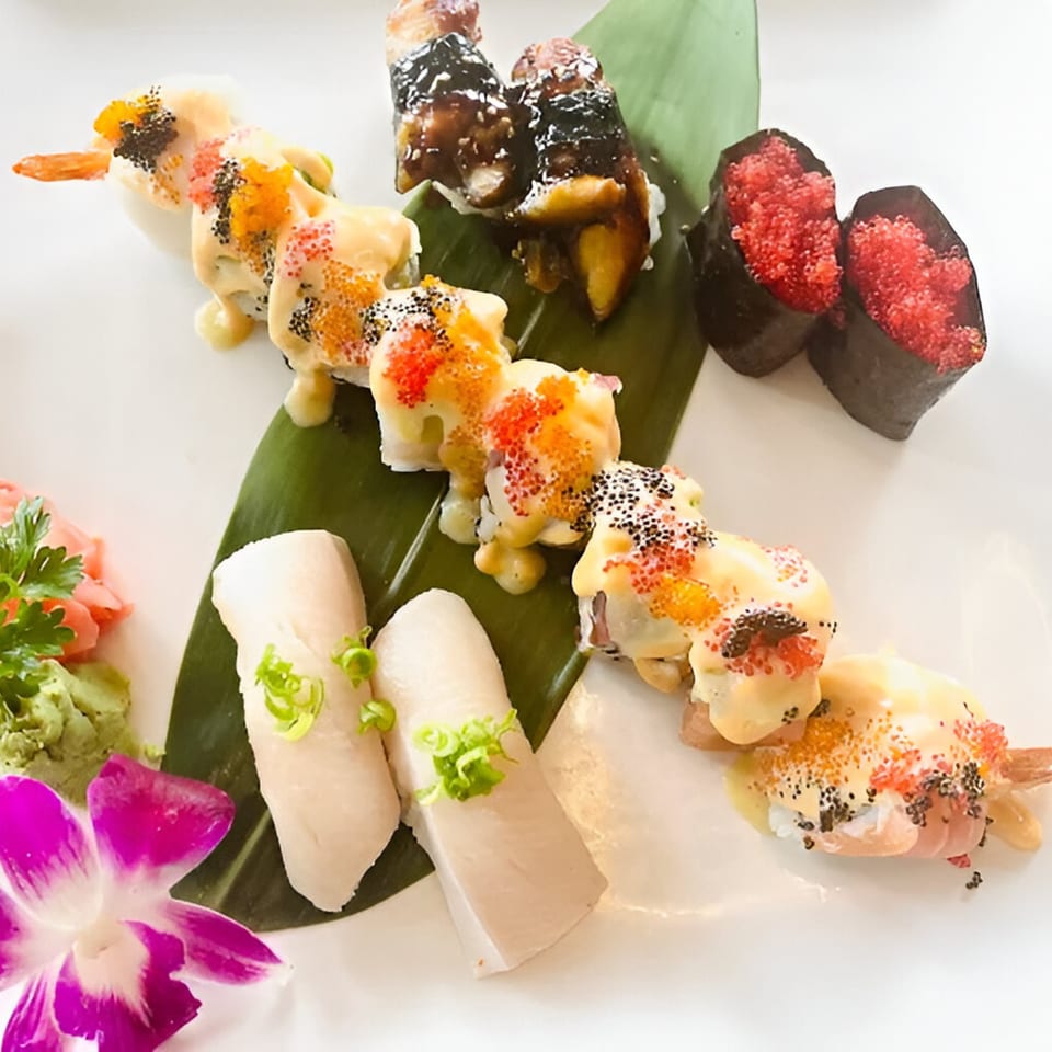 Assortment of Saisaki sushi rolls and nigiri, garnished with roe, sauce, and a purple orchid.
